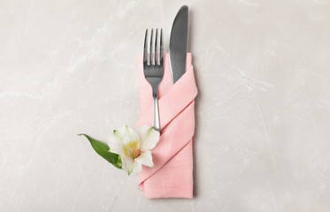 Folded napkin with fork, knife and flower on table, top view