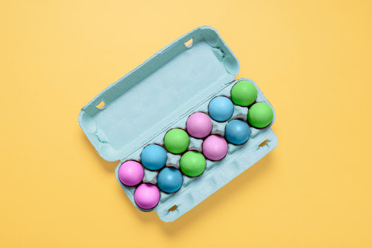 Top view of dozen dyed easter eggs in carton container.  Pastel painted easter eggs in egg crate on a bright pastel yellow background with copy space and room for text