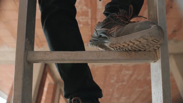 People working in construction site. Man at work in new house inside apartment building. Professional worker climbing ladder with safety shoes, using tool and equipment