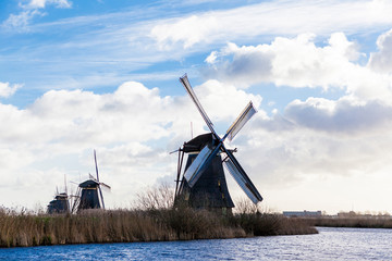 Traditional dutch windmill near the canal. Netherlands. Old windmill stands on the banks of the canal, and water pumps. White clouds on a blue sky, the wind is blowing. - 233397984