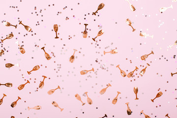 Party confetti sparkes in gold and white colors. There are small champagne glasses scrattered on the light pink background. Festive concept.