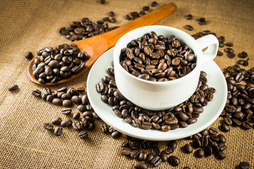 Cup full of coffee beans on the burlap background
