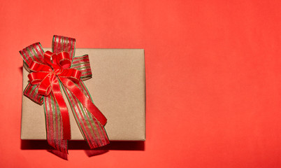 present box with red ribbon bow for Christmas, New Year, Valentine on red background, top view with copy space