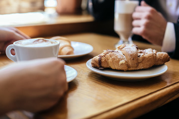 Drinking coffee with croissant on wooden table.