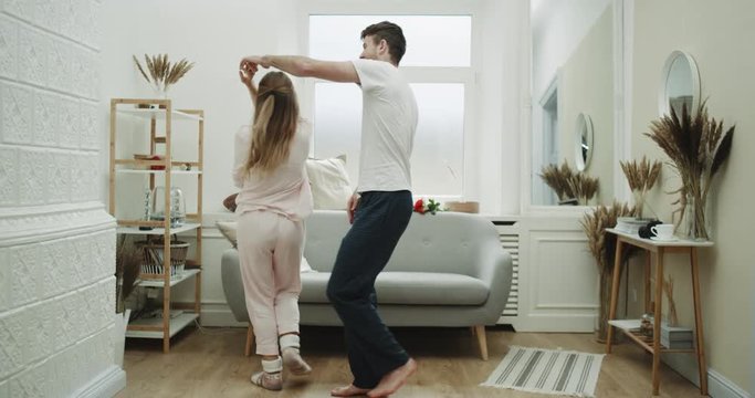 Happy couple in pajamas dacing in their cozy living room.