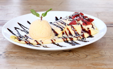 Closeup of vanilla ice cream with crepes and strawberry on wooden desk