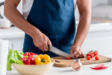 Obraz na płótnie Canvas partial view of man cutting cherry tomatoes on chopping board