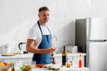 adult man in apron with glass of wine at kitchen