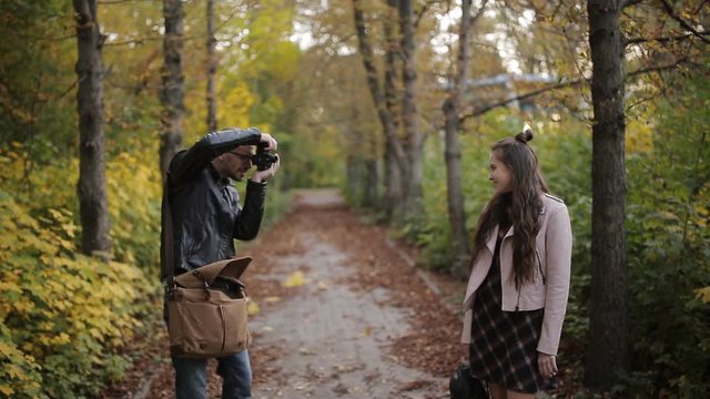 A photographer takes pictures of a teenager girl in autumn Park.