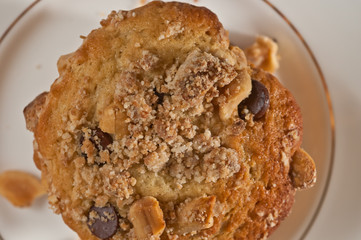 Top view, close up of a freshly baked, homemade peanut crumb chocolate chip muffins on a round, white, dish with a gold rim and a glass  of milk and a milk pitcher on a white table cloth