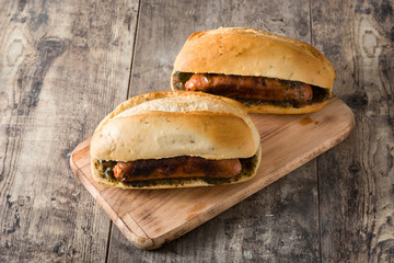 Choripan. Traditional Argentina sandwich with chorizo and chimichurri sauce on wooden table