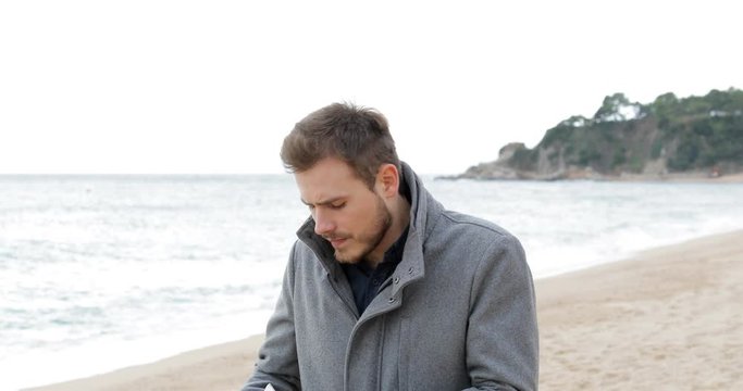 Ill man coughing in a cold day covering mouth with a tissue walking on the beach