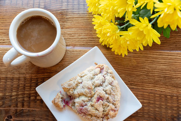 cozy scene of coffee, scone and yellow mum flowers on wooden table shot from overhead. 