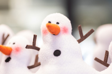 christmas holiday snowman decor. white crafted joined snow people with orange carrot noses and twig arms. shallow depth of field; bokeh background. 