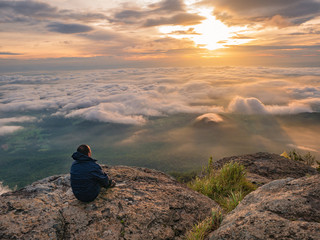 Trekker sitting on the mountain with Beautiful Sunrise and sea of mist in the morning on Khao Luang mountain in Ramkhamhaeng National Park,Sukhothai province Thailand