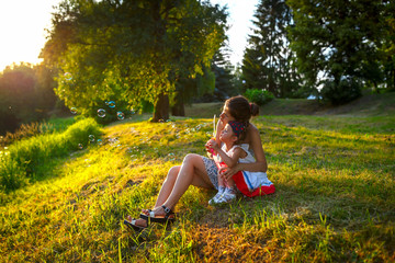 Mother and daughter inflate soap bubbles. Family portrait in backlight. Summer mood. Family time