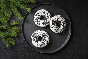 Donuts with white icing and chocolate chips in a black plate on the black kitchen table. Doughnuts on a plate. Delicious pastries. Top view with space for text