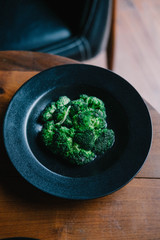 Broccoli on  black ceramic plate on wood table from above. Food photography concept, vibrant color, minimalism design style. Copy space