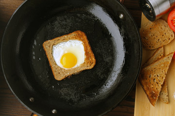 Fried eggs in bread in a pan, tomato and pepper on the table.