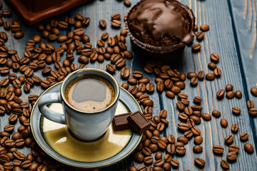 Cup of coffee on a blue wooden table with coffee beans and a chocolate.