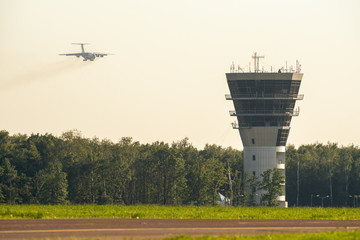 Fototapeta premium Airport control tower and commercial airplane landing at sunset