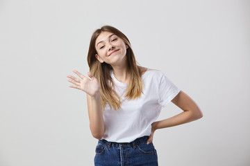 Friendly girl dressed in a white t-shirt and jeans shows hi on a white background in the studio