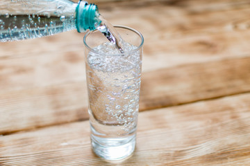 Sparkling water is poured into a glass on a wooden background.