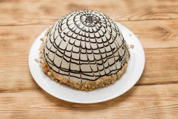 Cream cake sprinkled with spherical chocolate on a wooden background.