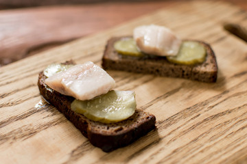 Sandwich from black bread with butter and herring on a wooden background.