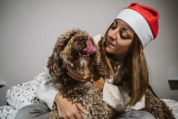 .Young, funny and happy woman playing with her nice brown spanish water dog. Celebrating Christmas time and wearing tematic costumes. Lifestyle.
