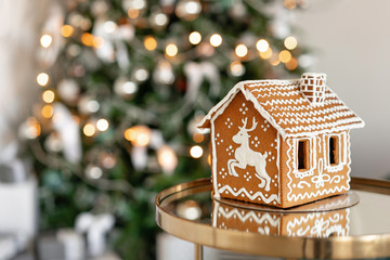 Gingerbread house on table. Defocused lights of Christmas tree. Morning in the bright living room....