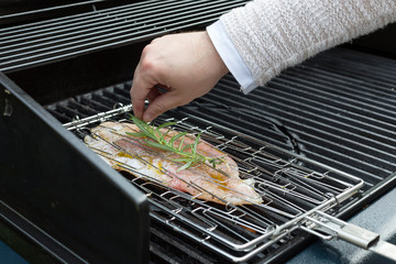 Mann garniert den Grillfisch im Grillgitter mit Thymian
