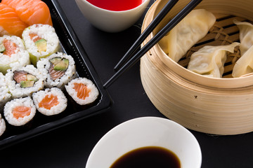 Dumplings or gyoza served in traditional steamer and sushi on black background. Close up