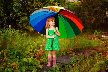 Happy child girl walk with multicolored umbrella under rain
