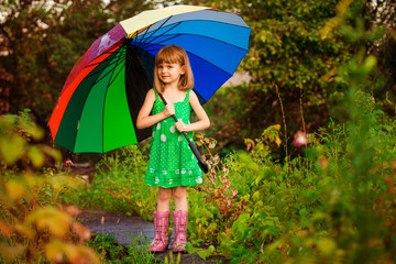 Happy child girl walk with multicolored umbrella under rain