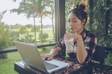 Young asia woman sitting alone at coffee shop working on a laptop