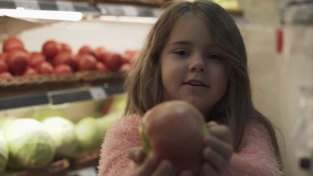 Smiling girl with an apple in hand on the background of shelves with fruit