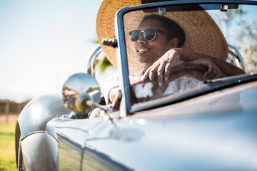 Black woman driving a vintage convertible car - obrazy, fototapety, plakaty