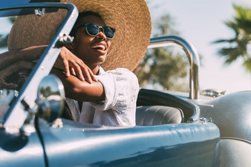 Black woman driving a vintage convertible car - obrazy, fototapety, plakaty