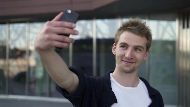 Cheerful caucasian man standing in the street and taking a selfie. Handheld real time medium shot