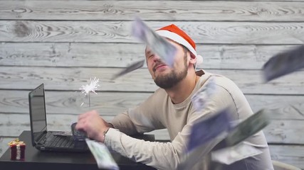 dreamy man in a christmas hat with bengal fire sparkler and laptop in his hands. Falling Money Dollars.