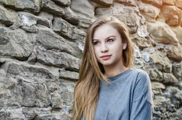 Attractive girl with long blond hair is looking to the left against a wall of stone background. Youth sexuality. Fashionable girl. PHOTO on a journey. Tourism in Europe.