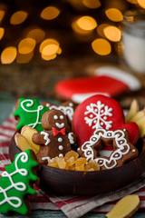 Fototapeta na wymiar Gingerbread mittens, little man, snowflakes, christmas trees in a brown wooden plate and a bottle of milk on a green wooden on the background of blurred garland. close up. space