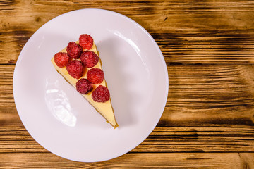 White plate with cheesecake New York and raspberries on wooden table. Top view