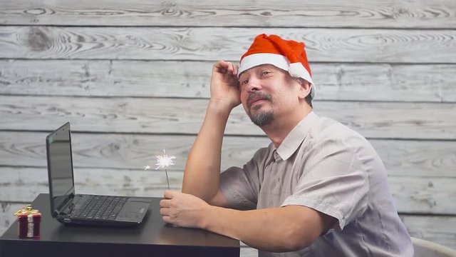 dreamy man in a christmas hat with bengal fire sparkler and laptop in his hands. Falling Money Dollars.