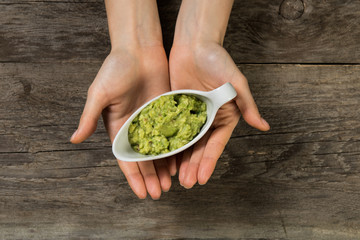 Beautiful woman hands holding grave boat with guacamole sauce on wooden background top view closeup