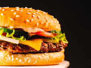 Juicy beef burger with cutlet, onion, vegetables, melted cheese, lettuce, sauce and topped sesame seeds. Isolated hamburger rotates on dark smoke background, close-up view