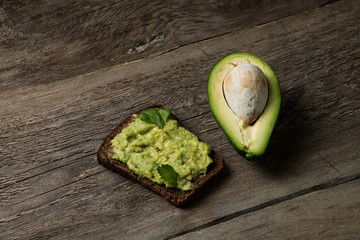 Bread with guacamole  sauce topping and piece of avocado on textured wood