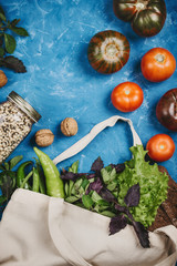 Flatlay of tomatoes, greens in eco bag and beans in a jar on blue background, zero waste groceries concept