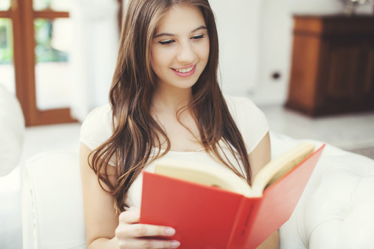 Happy Young Woman Reading Storybook On Couch At Home